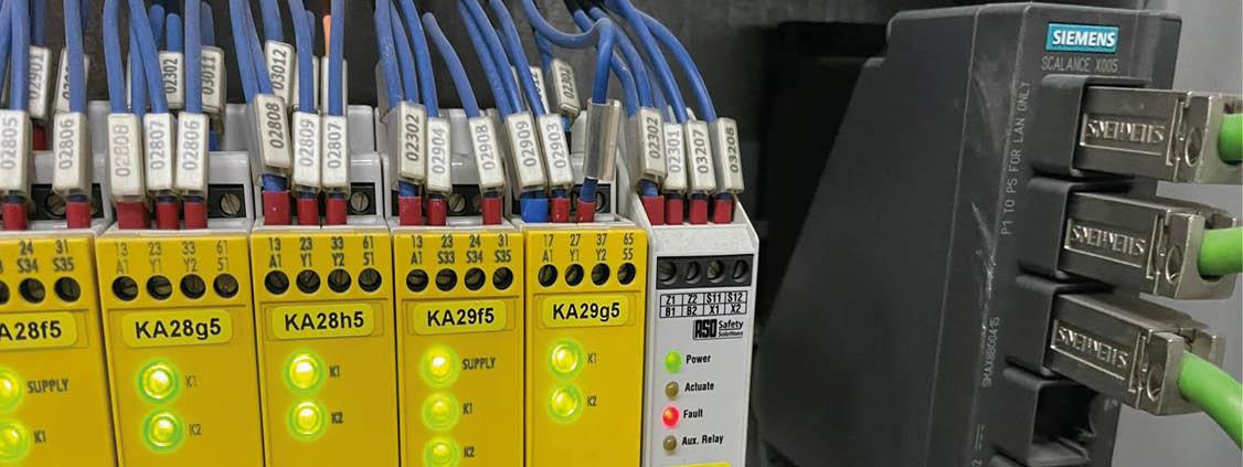 Close-up of industrial safety relays and a Siemens SCALANCE network switch with labeled wiring